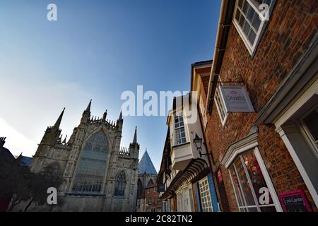 Das östliche Ende des York Minster von der College Street aus gesehen. Altmodische Backsteingebäude im Tudor-Stil überhängen die Straße unten. York, England. Stockfoto