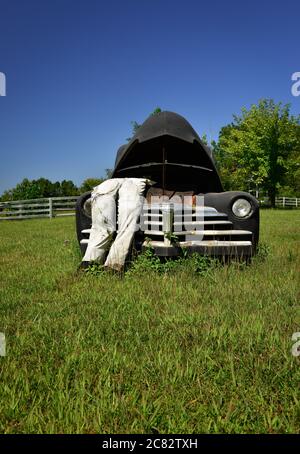 Niedriger Winkel EINER gefälschten Stadt Szene eines ausgestopften Dummy in Overalls lehnte in popped Haube auf alten 1930er-Auto in ländlichen grünen Feld in mittleren TN, USA Stockfoto