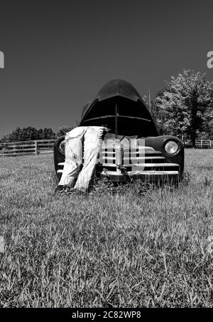 Eine gefälschte Stadtszene eines gestopften Dummy Mechaniker in Overalls lehnt sich über gepoppte Haube auf alten 1930er-Auto in ländlichen grün in Mittel TN, USA, Stockfoto