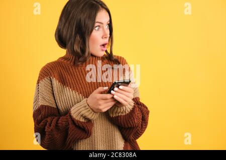 Überrascht Mädchen in Pullover mit Handy erstaunt Blick beiseite über gelben Hintergrund Stockfoto