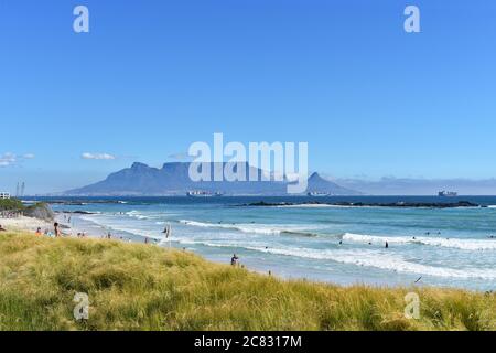 Tafelberg, Devils Peak und Lions Head vom Bloubergstrand Beach aus gesehen von der anderen Seite der Table Bay. Menschen können am Strand und im Wasser gesehen werden. Stockfoto