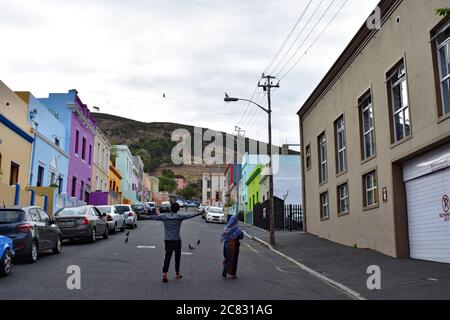 Ein männlicher und weiblicher Spaziergang in der Mitte der Straße hinauf zu den bunten Häusern der Bo-Kaap Gegend (Malaiisches Viertel) von Kapstadt. Stockfoto