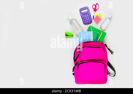Rucksack mit Schulbedarf und COVID 19 Vorbeugungsgegenständen. Draufsicht, auf weißem Hintergrund. Zurück zur Schule während Pandemie Konzept. Stockfoto