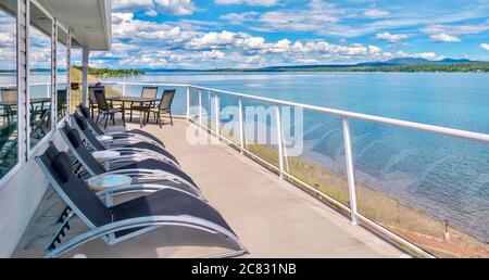 Großer privater Hausbalkon mit zeitgemäßem Glasgeländer und Terrassenmöbeln im Freien, mit Blick auf einen See in British Columbia, Kanada. Stockfoto