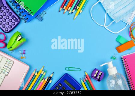 Schulbedarf und COVID 19 Vorbeugungsartikel. Rahmen auf blauem Papierhintergrund. Zurück zur Schule während Pandemie Konzept. Stockfoto