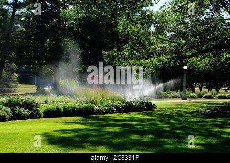 Sprinkler bewässern den Rasen und die Blumenbeete im Commissioners Park an einem heißen Sommermorgen in Ottawa, Ontario, Kanada. Stockfoto