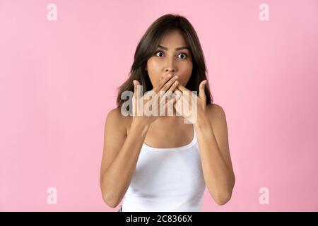 Überrascht junge Frau, die Kamera und den Mund mit Händen vor einem einfachen rosa Hintergrund Stockfoto