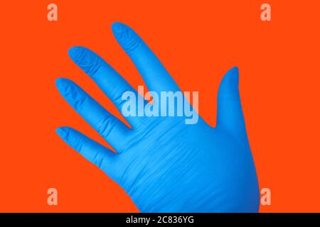 Menschliche Hand in Latex blau medizinischen Handschuh isoliert auf orange mit Geste. Schutzkonzept Stockfoto