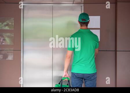 Delivery Mann Mitarbeiter in grünen Kappe T-Shirt bereit, Lieferung Lebensmittelbeutel vor dem kundenspezifischen Büro zu senden. Lieferung und Einkauf online Konzept. Stockfoto