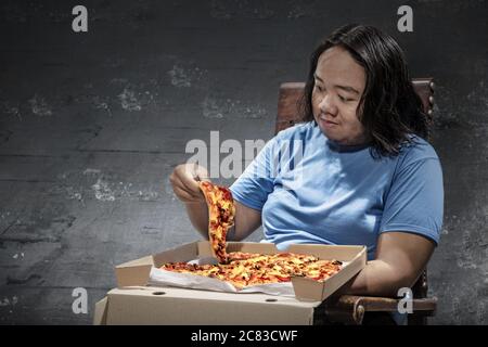 Asiatischer Mann, der zu Hause ein Stück Pizza isst. Junk-Food-Konzept Stockfoto