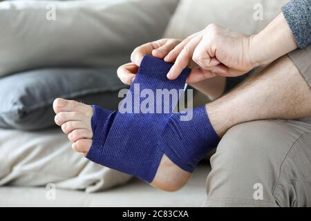 Mann sitzt auf der heimischen Couch und bandages Fuß Bandage Stockfoto