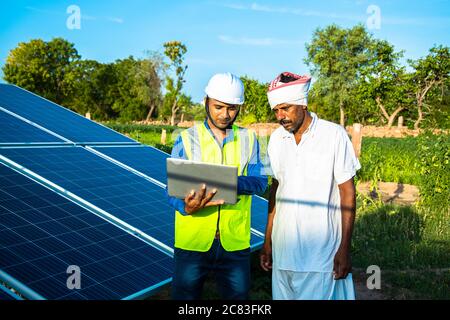 Junge Techniker überprüft die Wartung der Solarzellen und diskutieren mit Landwirt auf Feld, Technologie in der Landwirtschaft Stockfoto