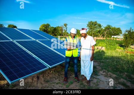 Junge männliche Techniker Arbeiter tragen grüne Westen und Helm überprüft die Wartung der Solarzellen und reden über die Installation von neuen Solarpanel Stockfoto