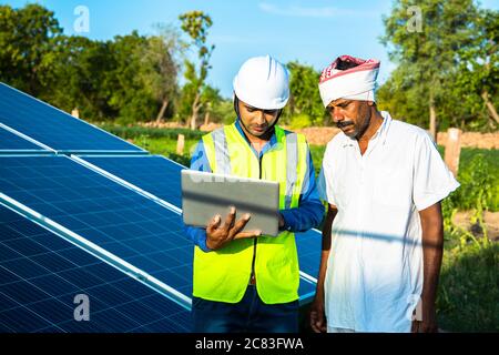 Junge männliche Techniker Arbeiter tragen grüne Westen und Helm überprüft die Wartung der Solarzellen und reden über die Installation von neuen Solarpanel Stockfoto