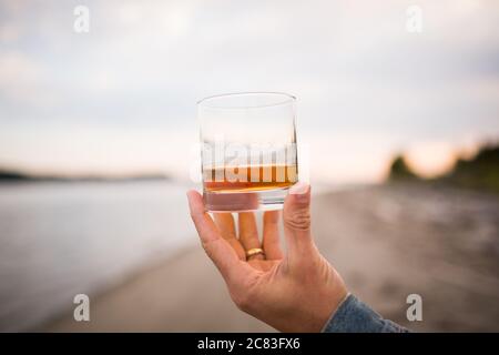Nahaufnahme einer männlichen Hand, die ein Glas hält Whiskey auf unscharfem Hintergrund Stockfoto