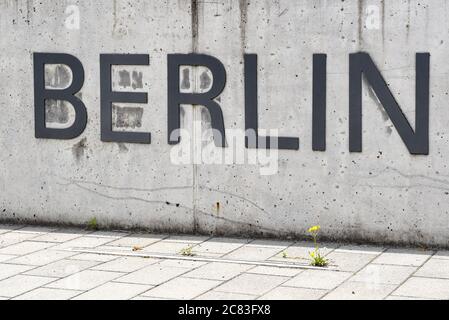 Berlin, Deutschland. Juli 2020. Das Wort "Berlin" ist an einer Betonwand vor einem Universitätsgebäude der Freien Universität in Dahlem angebracht. Davor wächst eine gelbe Blume vom Gehsteig. Sie ist Teil des Aufschrifteneindruckes 'Freie Universität Berlin'. Quelle: Jens Kalaene/dpa-Zentralbild/ZB/dpa/Alamy Live News Stockfoto