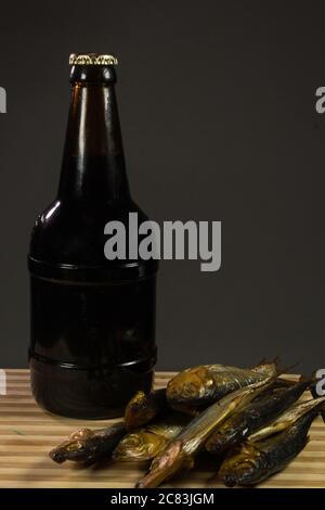 Eine Flasche dunkles Bier und ein Teller Fisch. Auf einem dunklen Hintergrund. Stockfoto