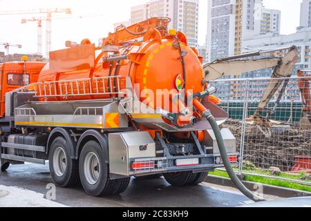 Pumpen von Wasser aus Kanalisation während des Baus von Straßen in der Stadt. LKW mit orangefarbenem Wassertank Stockfoto