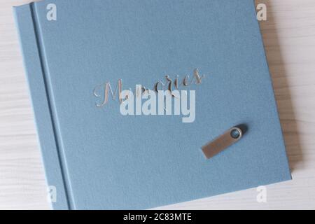 Blaues Textil-Fotobuch auf weißem Holztisch. Geschlossenes Fotobuch mit Flash-Laufwerk oben Stockfoto