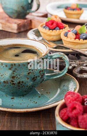 Schwarzer Kaffee in einer blauen Vintage-Tasse und Obsttörtchen mit Himbeeren und Heidelbeeren Stockfoto