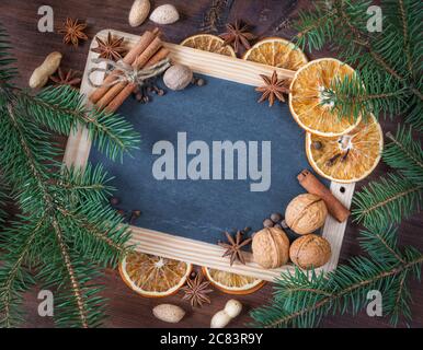 Leere Tafel, umgeben von grünen Tannenzweigen und verschiedenen Gewürzen als Weihnachtsrahmen mit Kopierraum Stockfoto