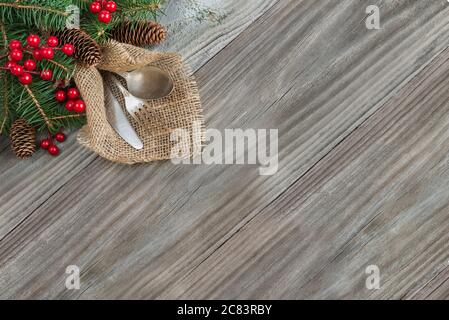 Weihnachtstisch mit Weihnachtsdeko: Altes Messer, Löffel und Gabel liegen auf der absackenden Serviette, sowie rote Stechbeeren und grüne Fichtenzweig, Stockfoto