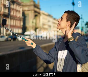 Der junge Mann mit Telefon ist auf der Straße einer Großstadt und winkt mit der Hand Stockfoto