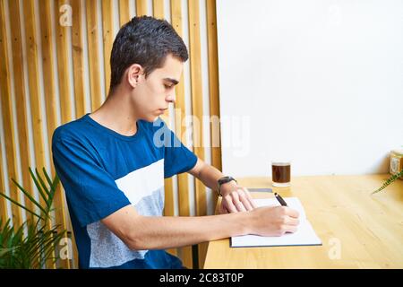 Junger Mann, der Informationen auf Notizblock schreibt, plant Teenager in legerer Kleidung einen Zeitplan Stockfoto