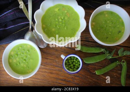 Frische grüne Erbsensuppe mit Erbsensamen und Erbsenschoten herum, Draufsicht Stockfoto