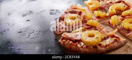 Gebackene hawaiianische Pizza mit Ananasscheiben, Mozzarella-Käse und Schinken auf einer dünnen, knusprigen Gebäckbasis, serviert auf einem Brett in einem Panorama-Banner mit CO Stockfoto