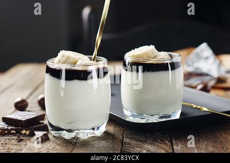 Milchdessert mit Banane und Schokoladencreme in einem Glas auf Holzgrund. Stockfoto