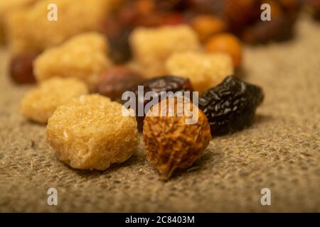 Stücke von braunem Rohrzucker und getrockneten Hagebutten auf einem homespun Tuch mit einer rauen Textur verstreut. Nahaufnahme Stockfoto