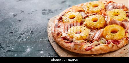 Tropische Hawaii-Pizza mit Ananasscheiben und Schinken auf einer Backplatte aus dem Ofen, serviert auf einem Brett in einem Panorama-Banner mit Copyspace Stockfoto