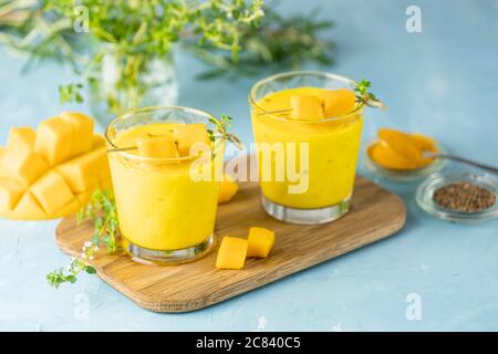 Gelber indischer Mango Joghurt Getränk Mango Lassi oder Smoothie mit Kurkuma und Safran. Gesundes probiotisches indisches kaltes Sommergetränk auf blauem Hintergrund Stockfoto