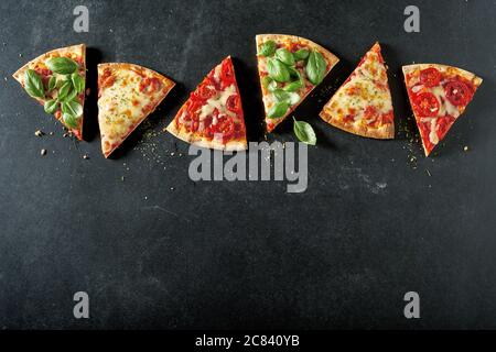 Portionen verschiedener leckerer italienischer Pizzen im Ofen mit verschiedenen Belägen und Beilagen, die als Rahmen auf Schiefer mit Copyspace dargestellt sind Stockfoto