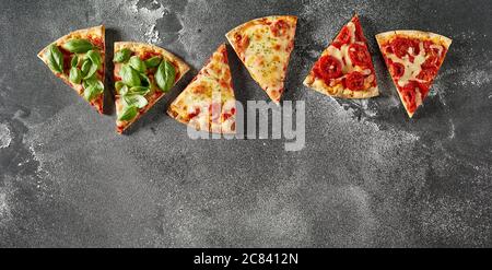 In Scheiben geschnittene Portionen italienische Pizza mit verschiedenen Besatz in einer Reihe als Rahmen auf einem bemehlten Schieferhintergrund mit Copyspace angeordnet Stockfoto