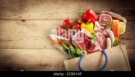 Panorama von Fleisch, Fisch und frischen Produkten in einem Einkaufstasche, das auf einen Holzhintergrund mit Vignette und Copyspace in einem gesunden Würfel ausläuft Stockfoto