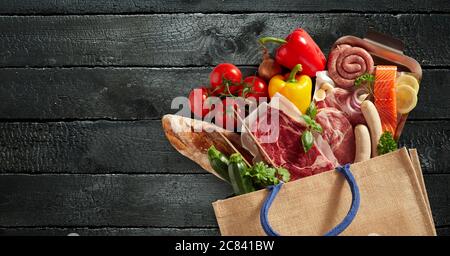 Wiederverwendbare Einkaufstasche mit frischen Lebensmitteln gefüllt, darunter verschiedene Fleisch-, Fisch-, Baguette-, Tomaten-, Paprika- und Kräuter-Sorten in einem flachen Stillleben Stockfoto