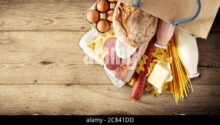 Einkaufstasche mit getrockneten italienischen Pasta und einer Auswahl an Milchprodukten, Eiern, Salami und würziger Wurst auf rustikalem Holzhintergrund mit Copypac Stockfoto