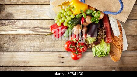 Frische Zutaten aus einem Einkaufstasche mit Gemüse, Trauben, würzigen Würsten und knusprigem Baguette auf einem rustikalen Holzpanorama Stockfoto