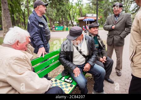 Chisinau / Moldawien - 15. Mai 2020: Gruppe erwachsener Männer, die auf einer grünen Bank im großen Park der Hauptstadt Moldawiens Schach spielen Stockfoto