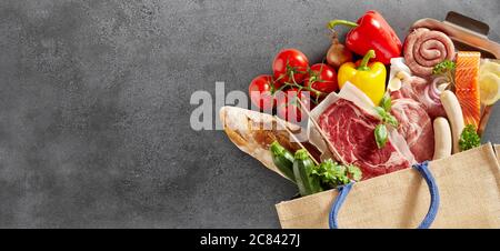 Nahaufnahme von frischen Lebensmitteln in einer Einkaufstasche über einem strukturierten Schieferhintergrund frische Lebensmittel einschließlich gemischtes Fleisch, Fisch, Baguette, Tomaten, Swee Stockfoto