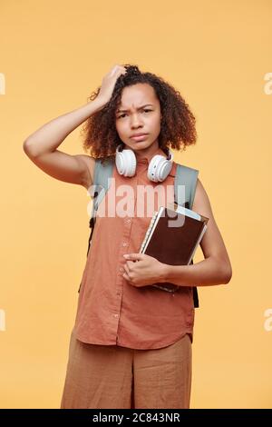 Portrait von verwirrt runzelig schwarz Student Mädchen in lässigen Outfit stehen mit Büchern und kratzen Kopf in Verwirrung Stockfoto