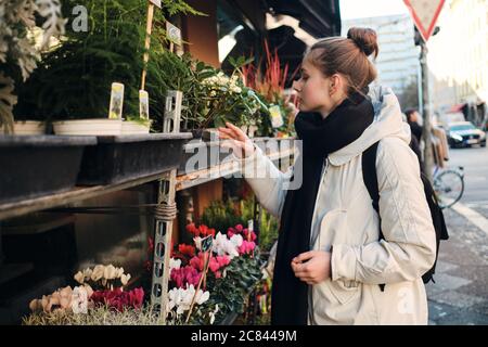 Seitenansicht der attraktiven casual Mädchen in Daunenjacke traumhaft wählen Blumen auf der Stadt Straße Stockfoto