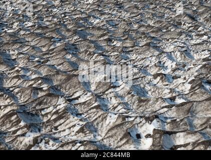 Nahaufnahme von Schneedünen mit schwarzem vulkanischem Lavasand mit Spiegelung des blauen Himmels. Island natürliche abstrakte Hintergrundtextur Stockfoto