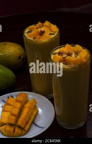 Köstliches Mango Lassi Getränk mit Mangopulpe Rosinen Mandeln und reifen Mango im Hintergrund Mango-Scheibe im Vordergrund dekoriert. Selektiver Fokus. Stockfoto
