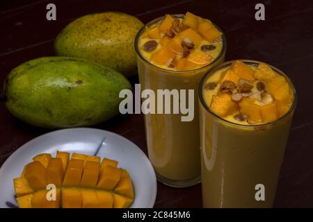 Köstliches Mango Lassi Getränk mit Mangopulpe Rosinen Mandeln und reifen Mango im Hintergrund Mango-Scheibe im Vordergrund dekoriert. Selektiver Fokus. Stockfoto