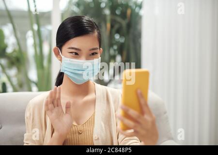 Casual Krankheit Frau trägt Maske und Video-Anrufe mit dem Smartphone zu Hause, Stockfoto