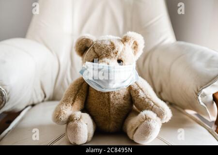 Ein Teddybär eines Kindes sitzt auf einem Stuhl und trägt eine Gesichtsmask Stockfoto