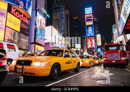 Ein gelbes Taxi in New York City in der belebten Times Square Street in der Nacht. Schilder und Anzeigen an Wolkenkratzerfassaden leuchten auf Autos Stockfoto